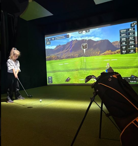 Une jeune golfeuse frappe une balle devant l'écran du simulateur